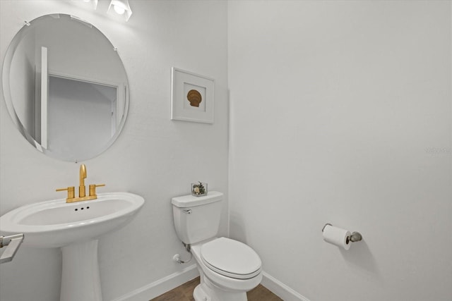 half bathroom with baseboards, a sink, and toilet