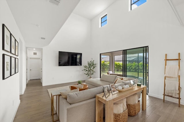 living area featuring a towering ceiling, wood finished floors, visible vents, and baseboards