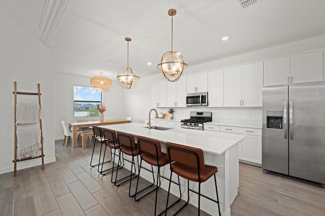 kitchen featuring appliances with stainless steel finishes, a kitchen island with sink, light countertops, pendant lighting, and a sink