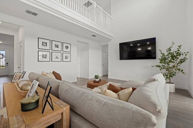 living area featuring a towering ceiling, wood finished floors, visible vents, and baseboards