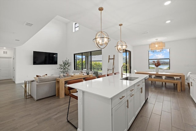 kitchen featuring a sink, white cabinets, light countertops, hanging light fixtures, and an island with sink