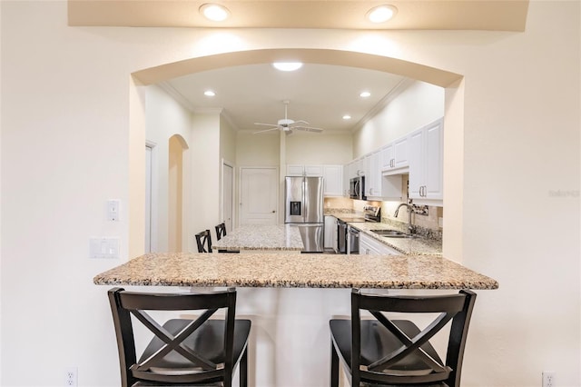 kitchen featuring white cabinetry, a kitchen bar, kitchen peninsula, appliances with stainless steel finishes, and backsplash