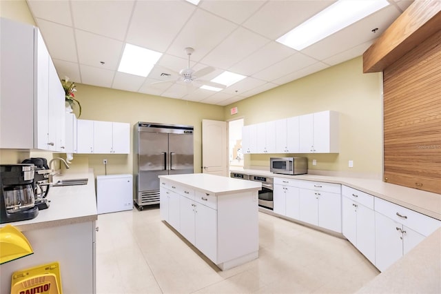 kitchen with a kitchen island, wooden walls, a paneled ceiling, stainless steel appliances, and white cabinets