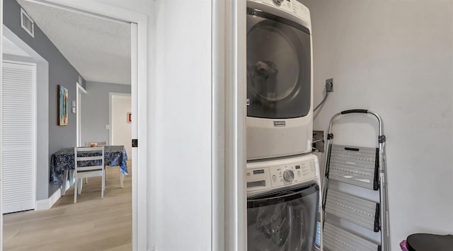 laundry area featuring light hardwood / wood-style floors, a textured ceiling, and stacked washer and dryer