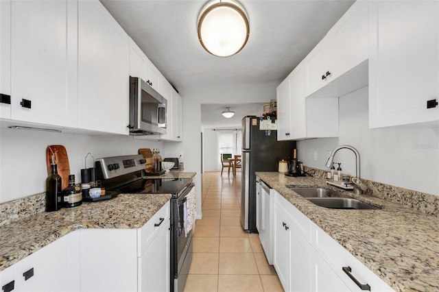 kitchen featuring white cabinets, appliances with stainless steel finishes, sink, light stone counters, and light tile patterned floors