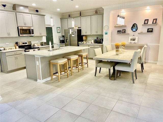 kitchen featuring sink, gray cabinetry, hanging light fixtures, a center island with sink, and appliances with stainless steel finishes