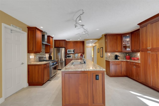 kitchen with sink, stainless steel appliances, light stone countertops, a kitchen island with sink, and backsplash