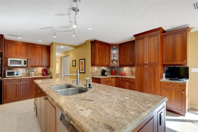 kitchen with light tile patterned flooring, sink, an island with sink, light stone countertops, and backsplash