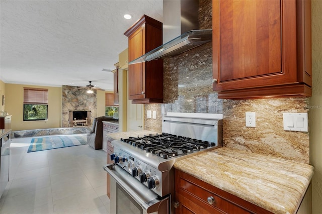 kitchen with wall chimney exhaust hood, tasteful backsplash, light stone counters, high end stainless steel range oven, and a fireplace