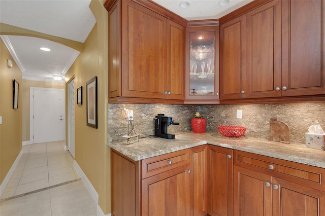 kitchen featuring tasteful backsplash, ornamental molding, light stone countertops, and light tile patterned flooring