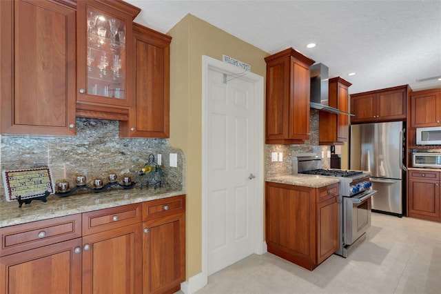 kitchen featuring appliances with stainless steel finishes, backsplash, light stone counters, and wall chimney exhaust hood