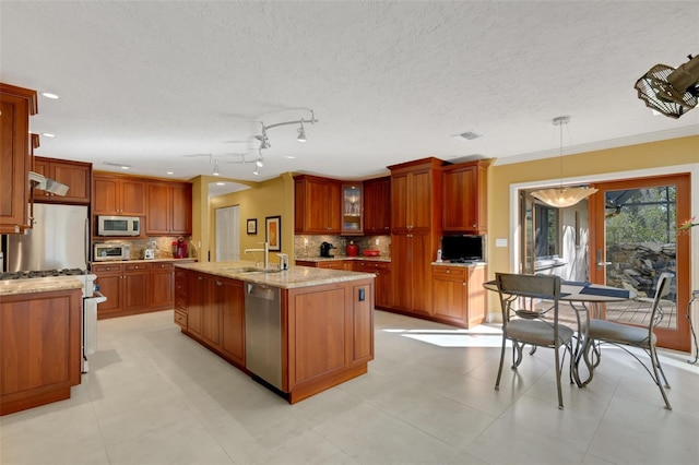 kitchen featuring appliances with stainless steel finishes, pendant lighting, backsplash, a kitchen island with sink, and light stone countertops