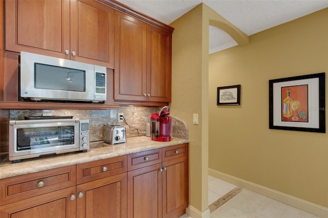 kitchen with decorative backsplash, light stone countertops, and light tile patterned flooring