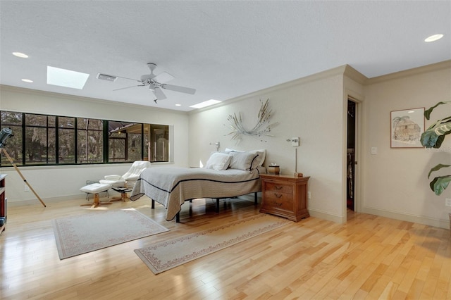 bedroom featuring ceiling fan, a skylight, ornamental molding, light hardwood / wood-style floors, and a textured ceiling