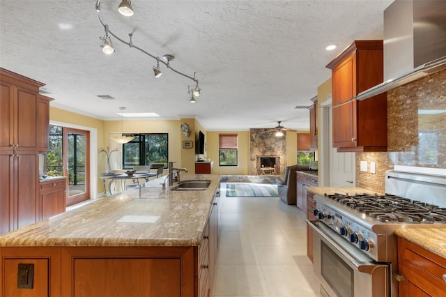 kitchen featuring light stone counters, a stone fireplace, stainless steel stove, and an island with sink