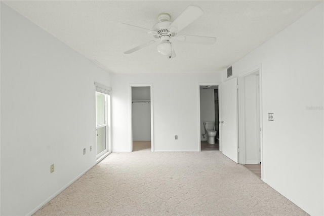 unfurnished bedroom featuring a walk in closet, a closet, ceiling fan, light colored carpet, and ensuite bathroom