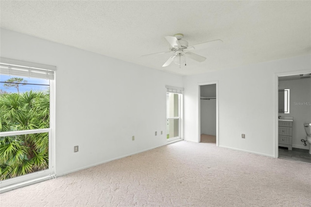 unfurnished bedroom with ceiling fan, light carpet, connected bathroom, and a spacious closet