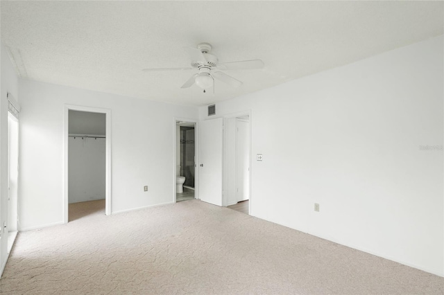 unfurnished bedroom with a spacious closet, a closet, carpet, ceiling fan, and connected bathroom