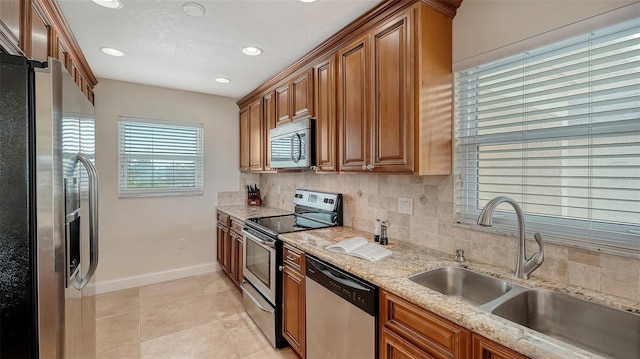 kitchen with sink, backsplash, light tile patterned floors, light stone counters, and stainless steel appliances