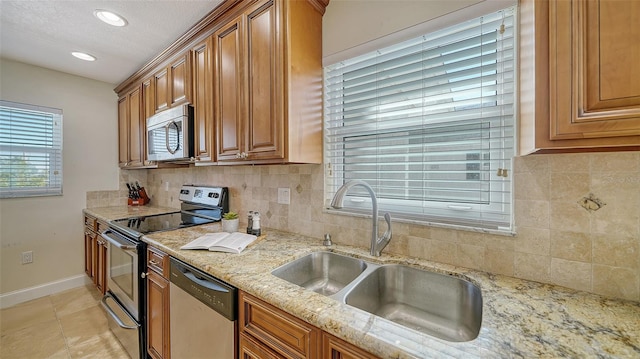 kitchen with light stone counters, stainless steel appliances, a sink, backsplash, and brown cabinetry