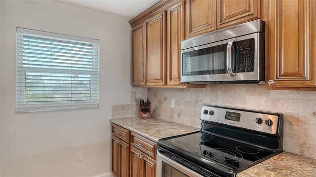 kitchen with brown cabinets, light stone counters, stainless steel appliances, and decorative backsplash