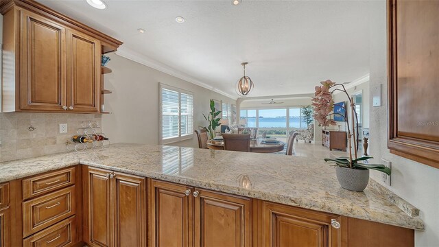 kitchen with hanging light fixtures, light stone countertops, brown cabinetry, and crown molding