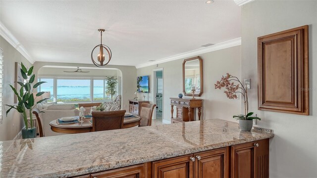 kitchen with crown molding, light stone counters, decorative light fixtures, and brown cabinets