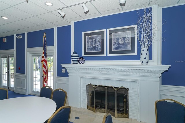 living area with a brick fireplace, a decorative wall, track lighting, and wainscoting