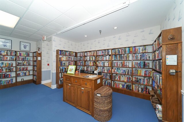 living area featuring wall of books, wallpapered walls, and a paneled ceiling