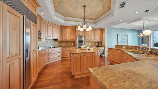 kitchen with a raised ceiling, a center island, built in appliances, pendant lighting, and sink