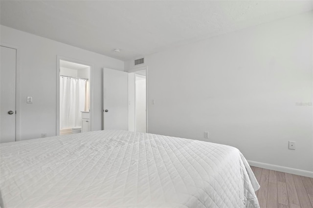 bedroom featuring visible vents, ensuite bath, light wood-style flooring, and baseboards