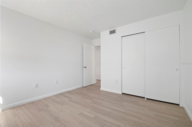 unfurnished bedroom with a closet, visible vents, a textured ceiling, light wood-type flooring, and baseboards