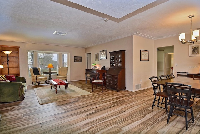 living room featuring light wood-type flooring, a notable chandelier, crown molding, and a textured ceiling