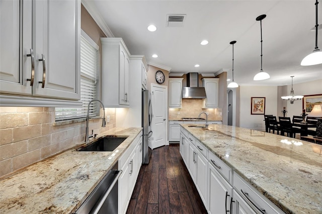 kitchen with wall chimney exhaust hood, sink, pendant lighting, stainless steel appliances, and white cabinets