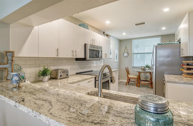 kitchen featuring appliances with stainless steel finishes, white cabinetry, light stone counters, decorative backsplash, and kitchen peninsula