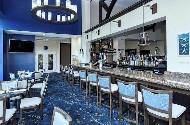 bar featuring a towering ceiling, white cabinets, dark stone counters, hanging light fixtures, and dark colored carpet