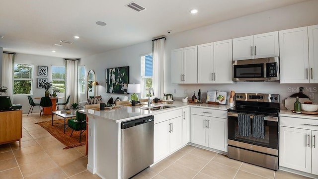 kitchen featuring kitchen peninsula, sink, light tile patterned floors, appliances with stainless steel finishes, and white cabinets