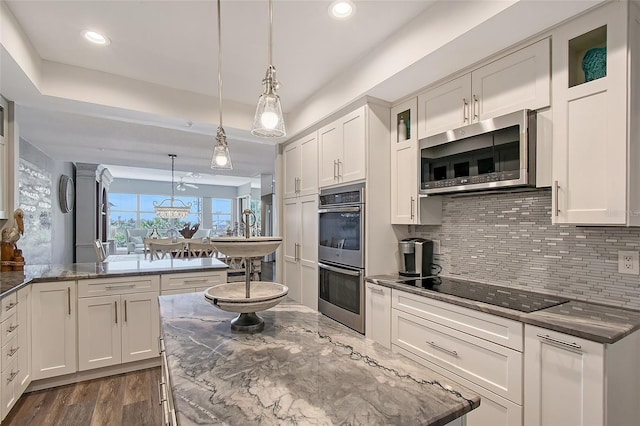 kitchen with appliances with stainless steel finishes, white cabinets, dark stone counters, and decorative light fixtures