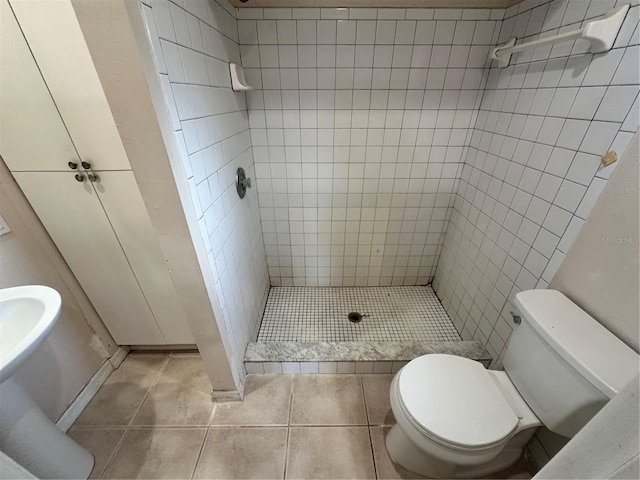 bathroom with toilet, a tile shower, and tile patterned flooring