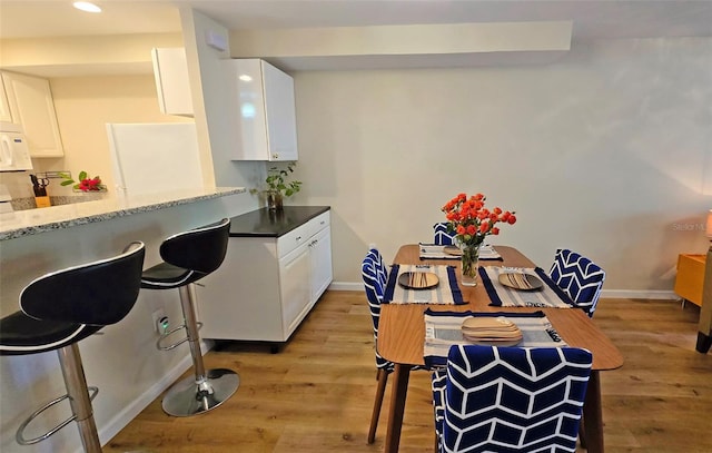 kitchen featuring hardwood / wood-style flooring, kitchen peninsula, white cabinets, and a kitchen bar