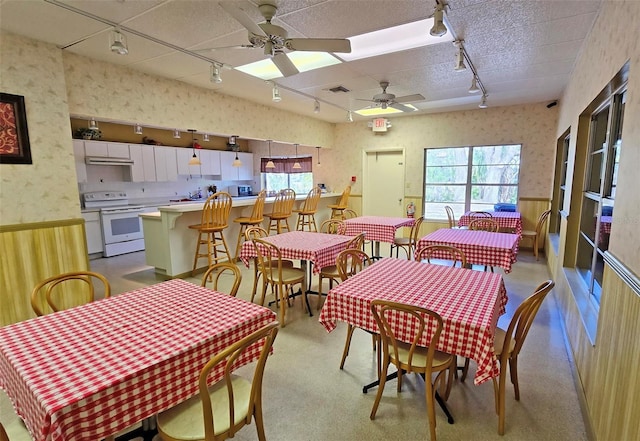 dining space with plenty of natural light, ceiling fan, and wood walls