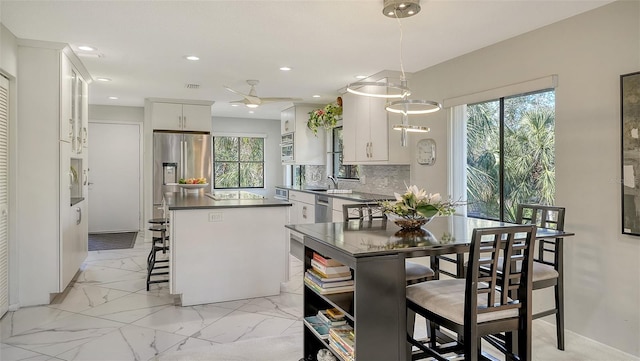 kitchen featuring tasteful backsplash, decorative light fixtures, appliances with stainless steel finishes, a kitchen island, and white cabinets