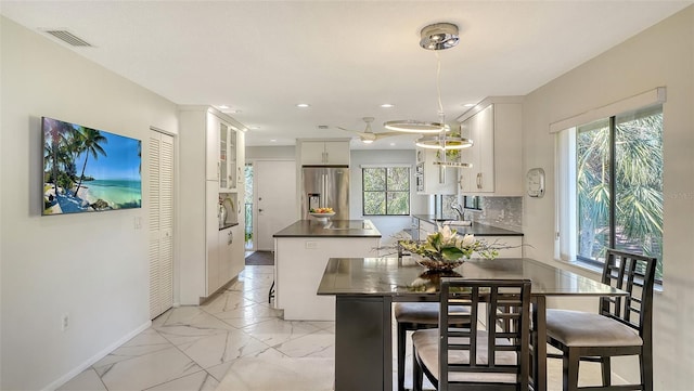 kitchen featuring white cabinetry, a kitchen breakfast bar, decorative backsplash, hanging light fixtures, and stainless steel refrigerator with ice dispenser