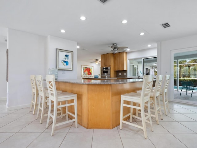 kitchen featuring a kitchen breakfast bar, light tile patterned floors, ceiling fan, kitchen peninsula, and stainless steel double oven