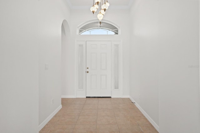 entryway with light tile patterned floors, a chandelier, a towering ceiling, and ornamental molding