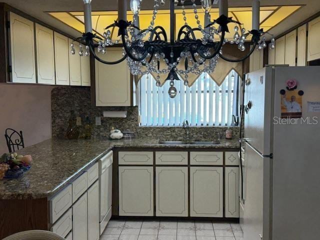 kitchen featuring tasteful backsplash, sink, white appliances, dark stone counters, and a chandelier