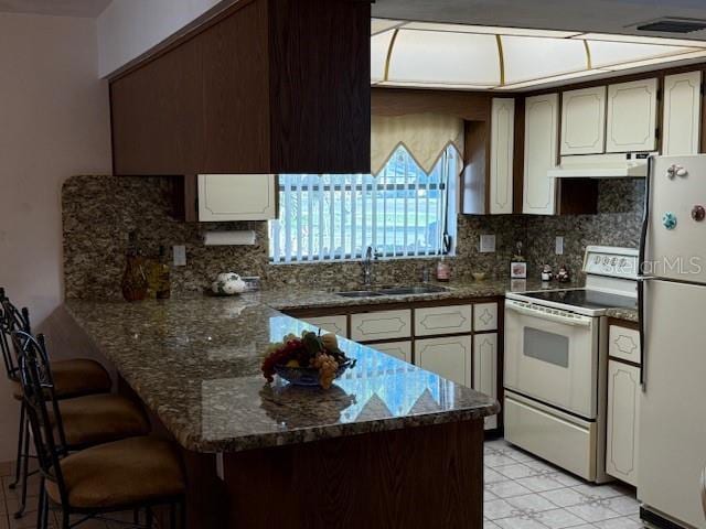 kitchen with kitchen peninsula, white range with electric stovetop, dark stone counters, refrigerator, and sink