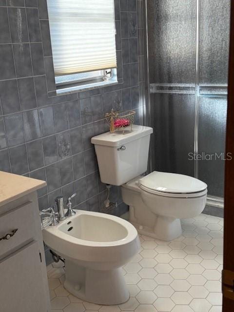 bathroom with a bidet, toilet, tile patterned flooring, and tile walls