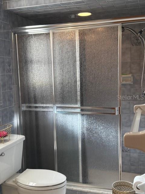 bathroom featuring a shower with shower door, tile walls, and toilet