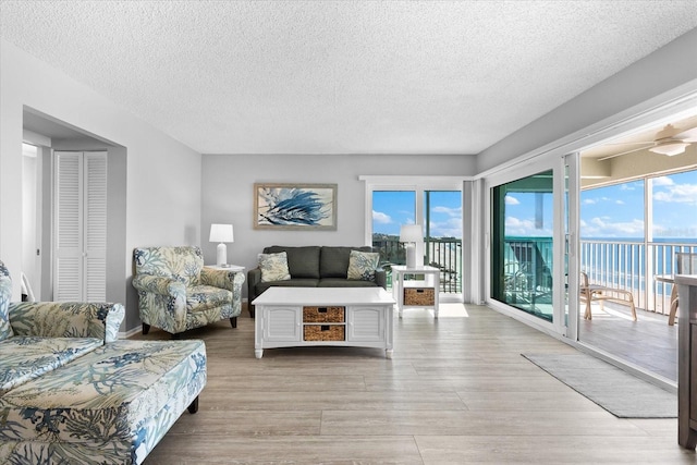 living room featuring a water view, plenty of natural light, a textured ceiling, and light wood-type flooring